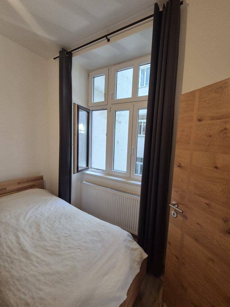 Schlafzimmer mit Einzelbett, Fenster und Heizung, ausgestattet mit Holzboden.