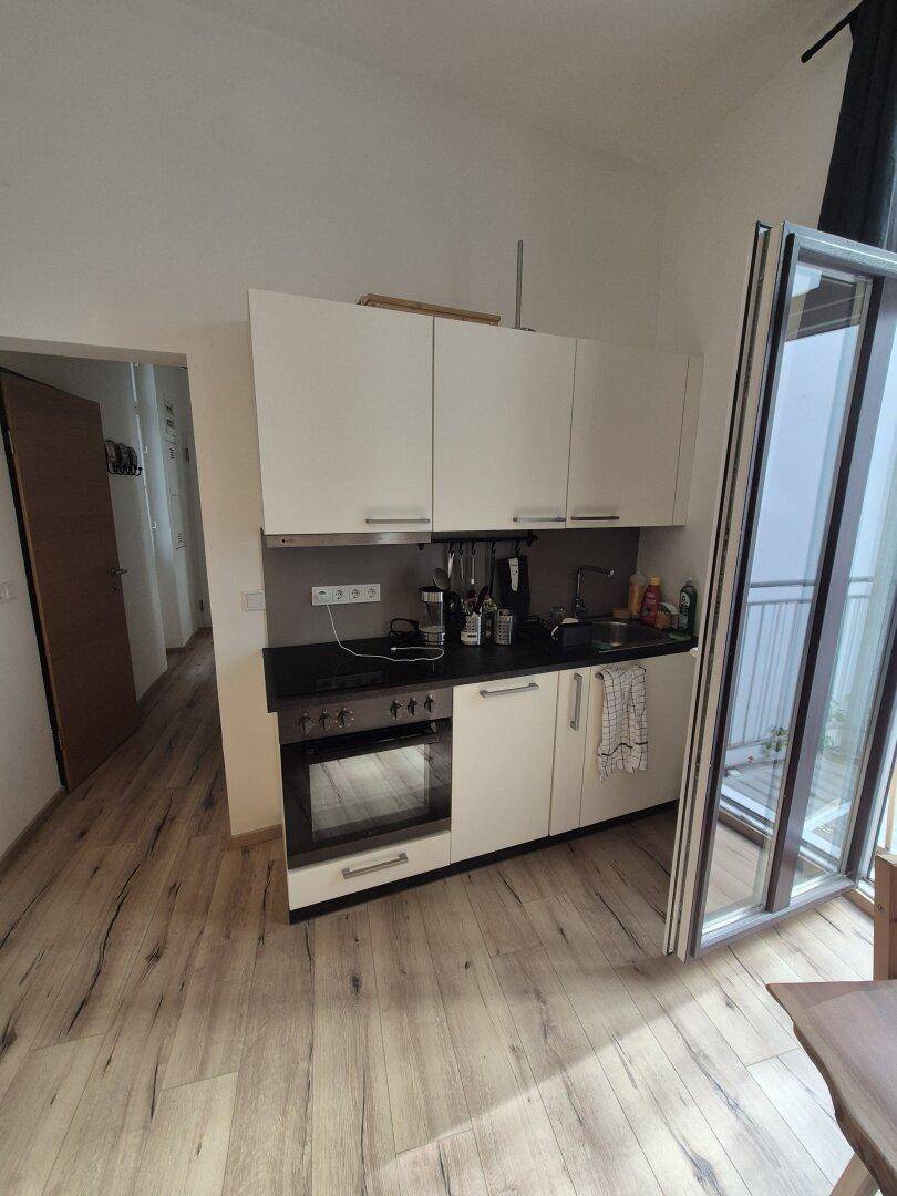 Kleine, funktionale Küchenzeile mit weißen Schränken und integriertem Backofen neben einem Fenster.