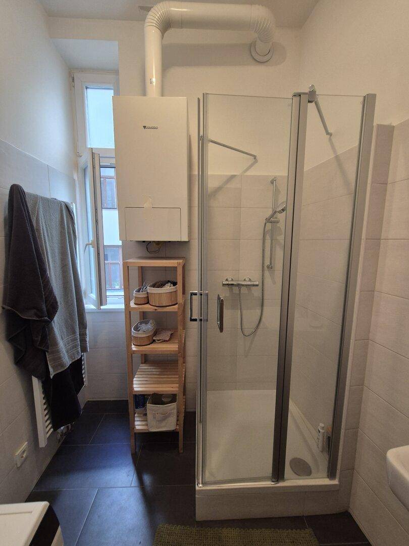 Modernes Badezimmer mit Duschkabine, Waschbecken und Fenster, ausgestattet mit hellen Fliesen.