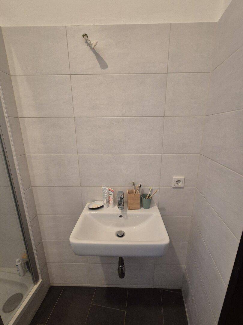 Modernes Waschbecken mit Spiegel und Ablagefläche in einem hell gefliesten Badezimmer.