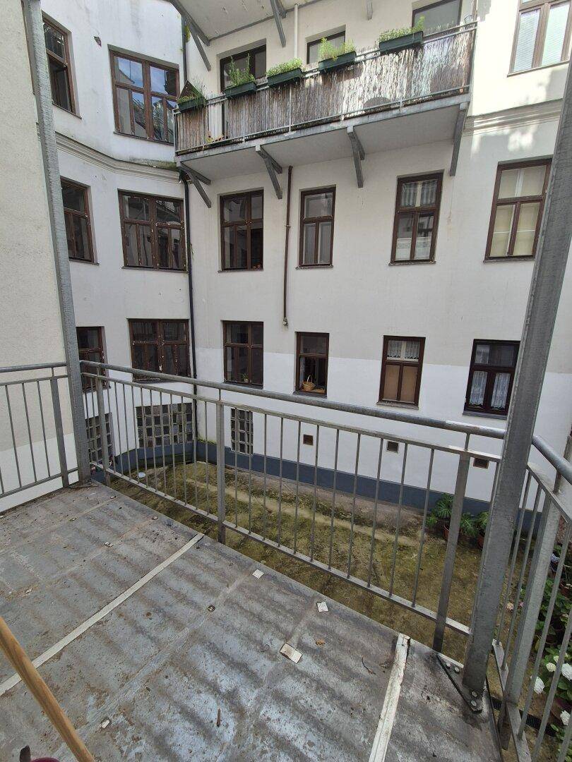 Kleiner Balkon mit Metallgeländer und Blick auf den Innenhof des Gebäudes.