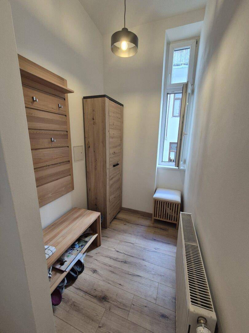 Eingangsbereich mit Garderobe, Schuhregal und Fenster, ausgestattet mit Holzboden.
