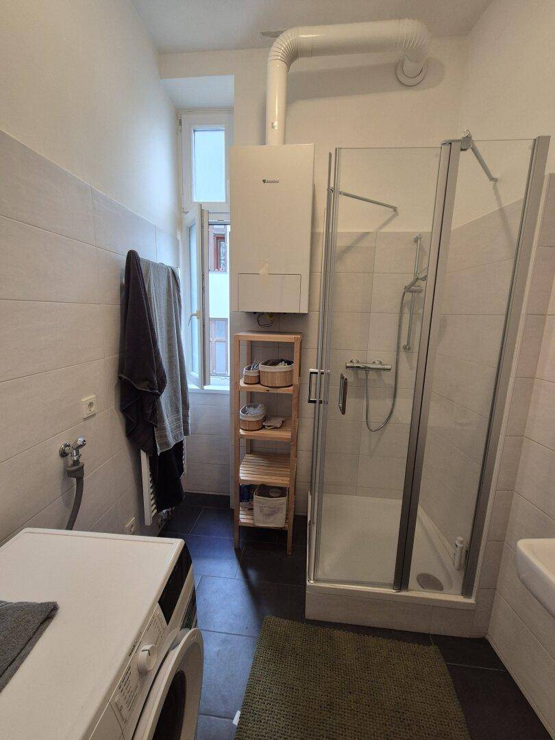 Helles Badezimmer mit Duschkabine, Waschmaschine und Fenster, ausgestattet mit modernen Fliesen.