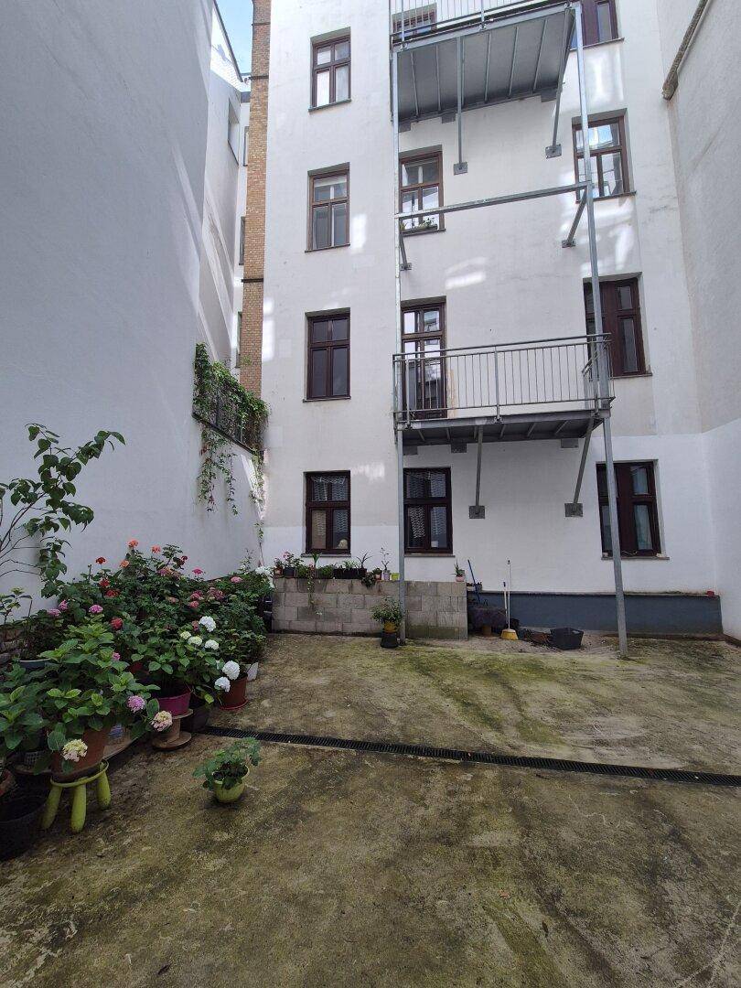 Innenhof mit Pflanzen und Blumen in Töpfen, umgeben von Gebäudefassaden.