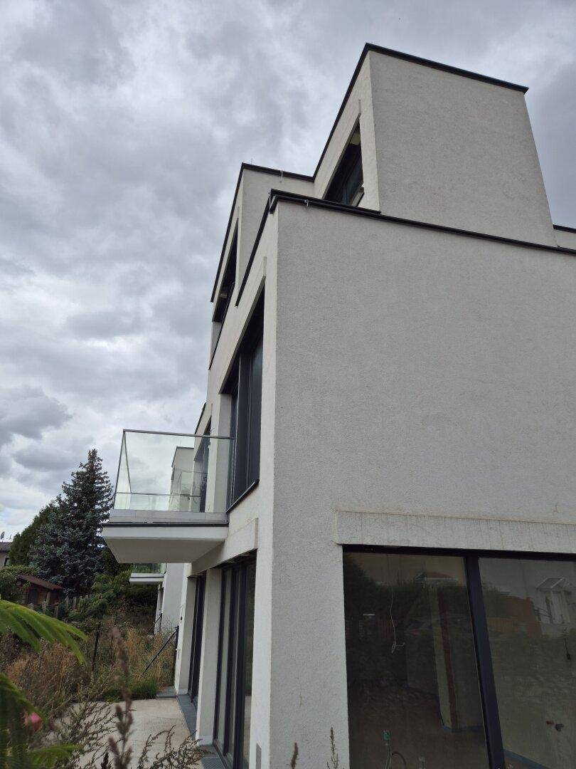 Seitenansicht eines modernen Gebäudes mit Balkon und großen Fenstern unter bewölktem Himmel.