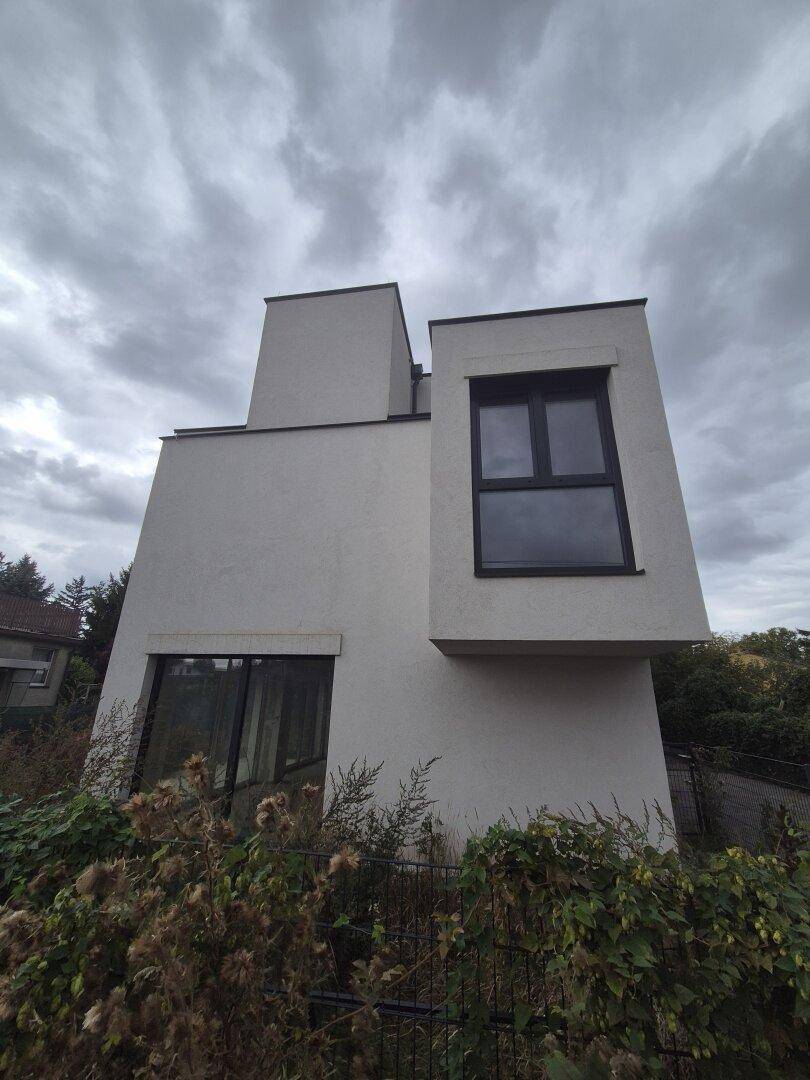 Ansicht eines modernen Gebäudes mit markanten Fenstern und minimalistischer Architektur unter bewölktem Himmel.