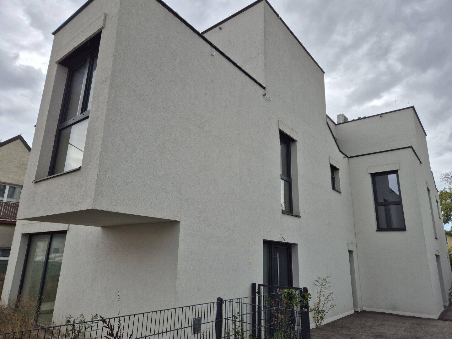 Rückansicht eines modernen Gebäudes mit markanter Architektur und verschiedenen Fensterformen.