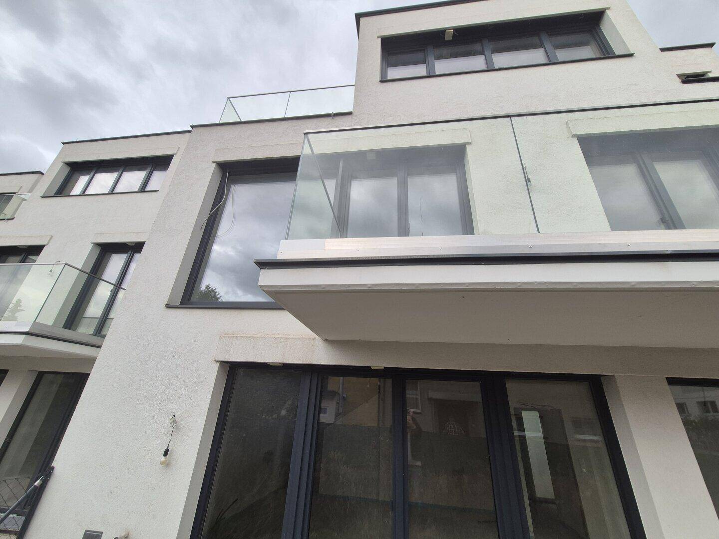 Nahaufnahme der modernen Fassade mit großen Fenstern und einem Balkon mit Glasgeländer.