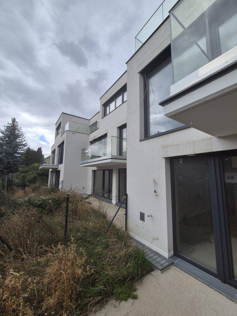 Mehrere moderne Balkone mit Glasgeländern an einer Wohnanlage unter bewölktem Himmel.