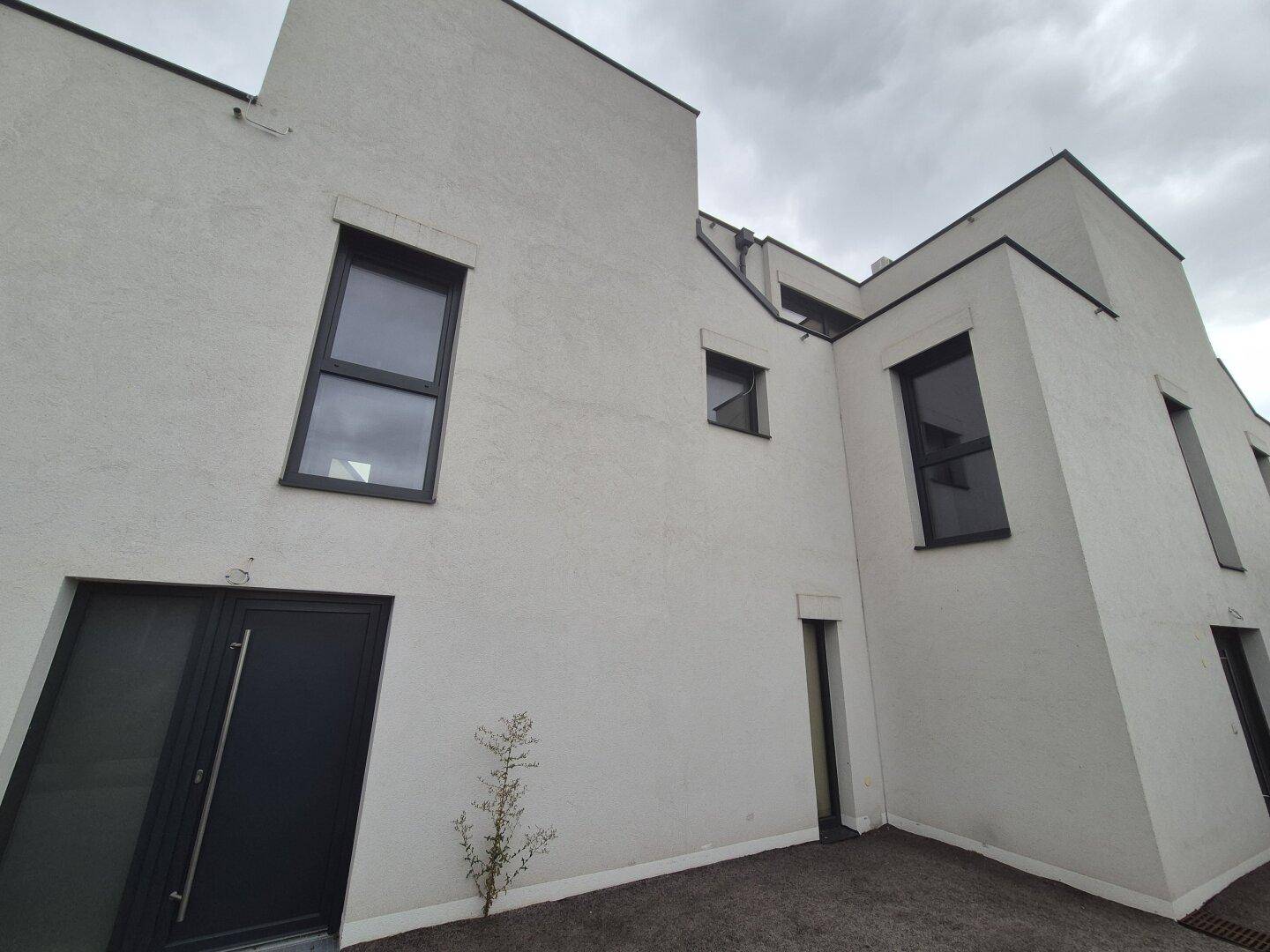 Moderne Gebäudefassade mit Eingangstür und verschiedenen Fenstergrößen unter bewölktem Himmel.