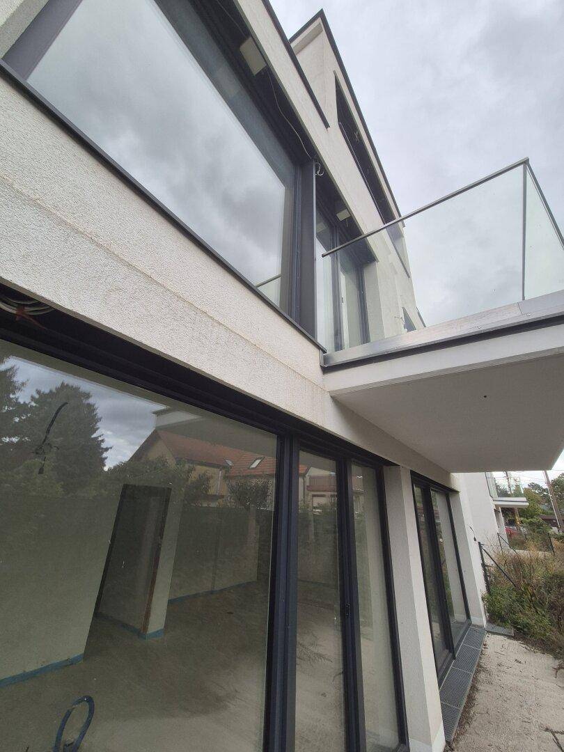 Nahaufnahme der modernen Fassade mit großen Fensterfronten und einem Balkon mit Glasgeländer.