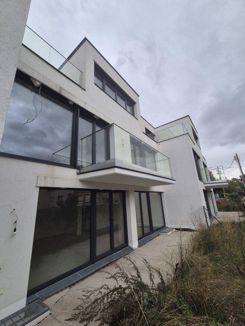 Moderne Wohnanlage mit mehreren Balkonen und großen Fensterfronten unter bewölktem Himmel.