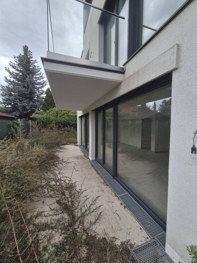 Seitenansicht eines modernen Gebäudes mit großen Fensterfronten und einem unfertigen Außenbereich.