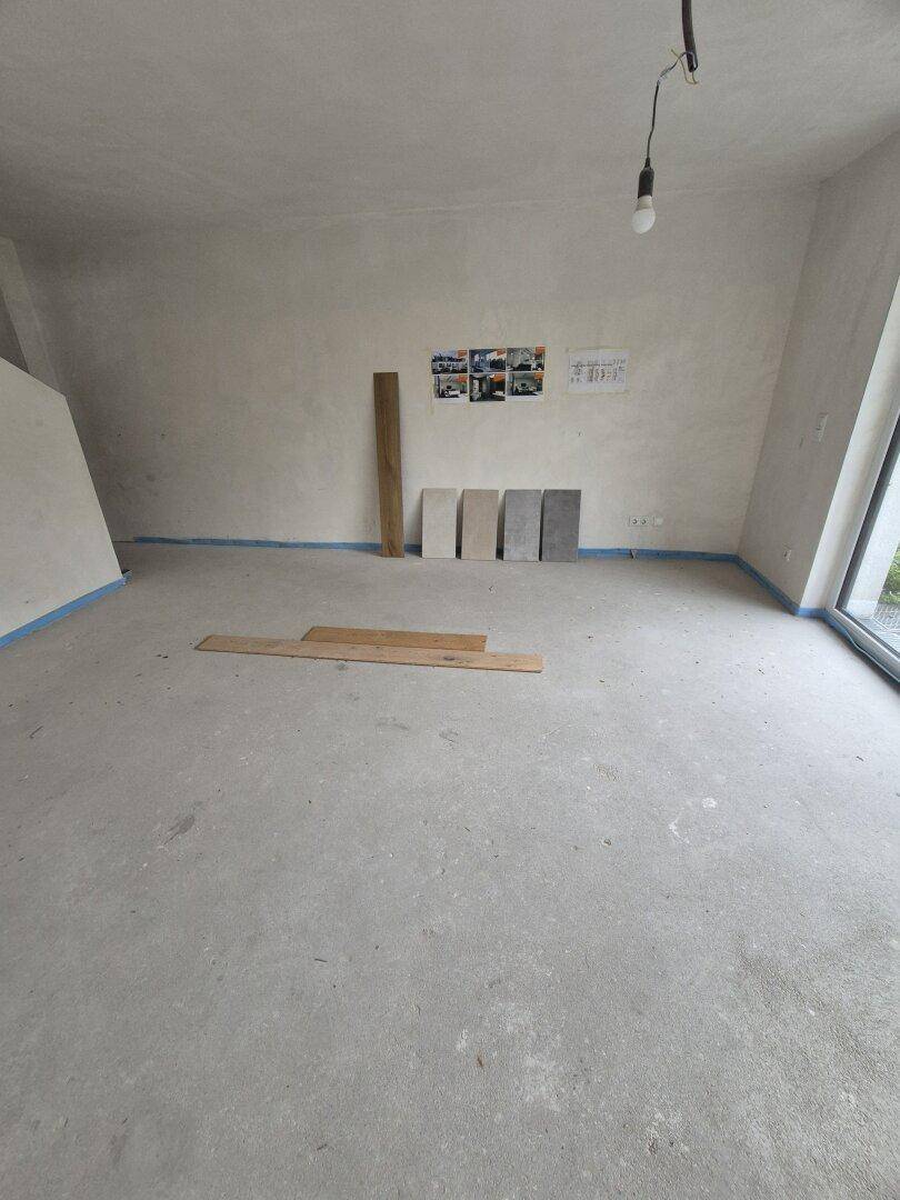 Unfertiger Innenraum mit Betonboden, ungestrichenen Wänden und Materialproben.