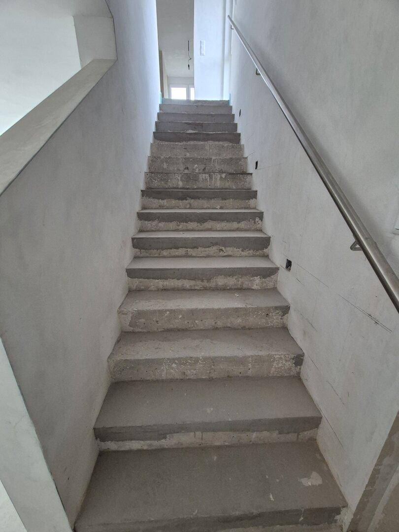 Unfertige Betontreppe mit Metallgeländer in einem Neubau, bereit für den weiteren Ausbau.