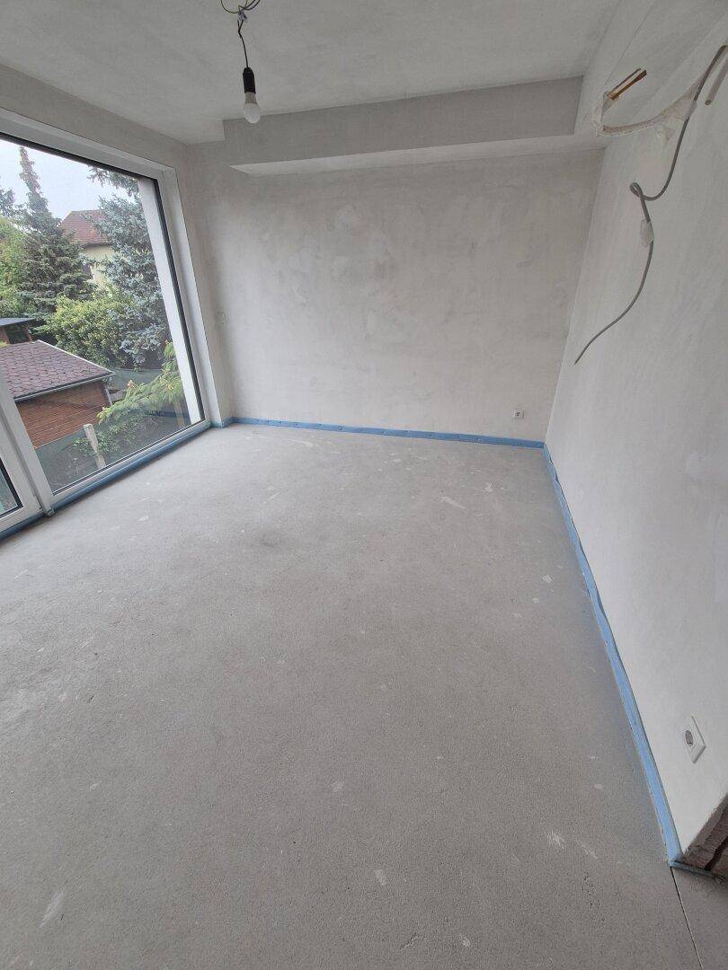 Unfertiger Innenraum mit großem Fenster und Blick ins Grüne, bereit für den weiteren Ausbau.