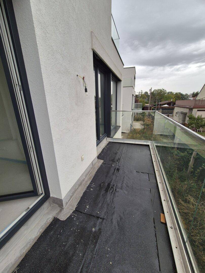 Unfertiger Balkon mit Glasgeländer und Blick auf die Umgebung, bereit für die Fertigstellung.