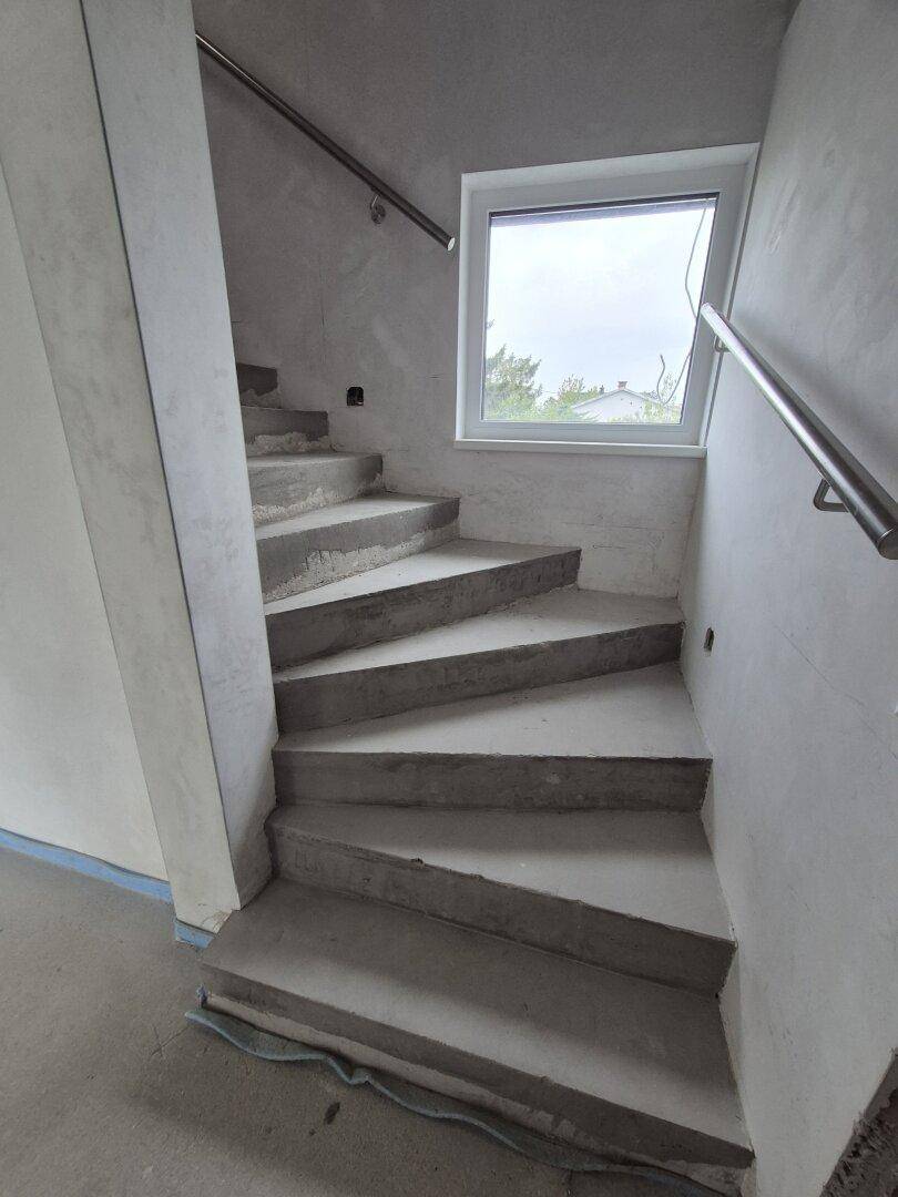Unfertige Betontreppe mit Fenster und Metallgeländer in einem Neubau.