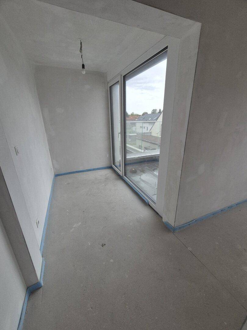 Unfertiger Innenraum mit großem Fenster und Blick auf die Umgebung, bereit für den Ausbau.