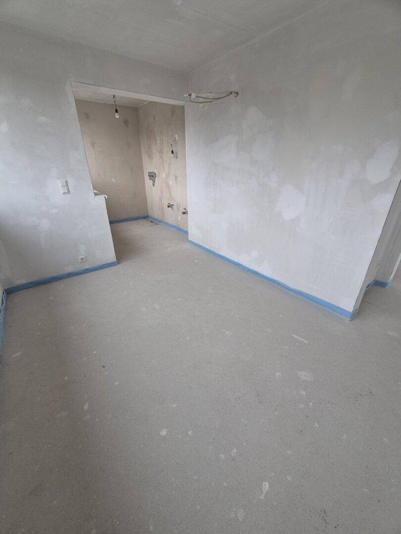 Unfertiger Innenraum mit Rohbauwänden und Betonboden, bereit für den weiteren Ausbau des Gebäudes.