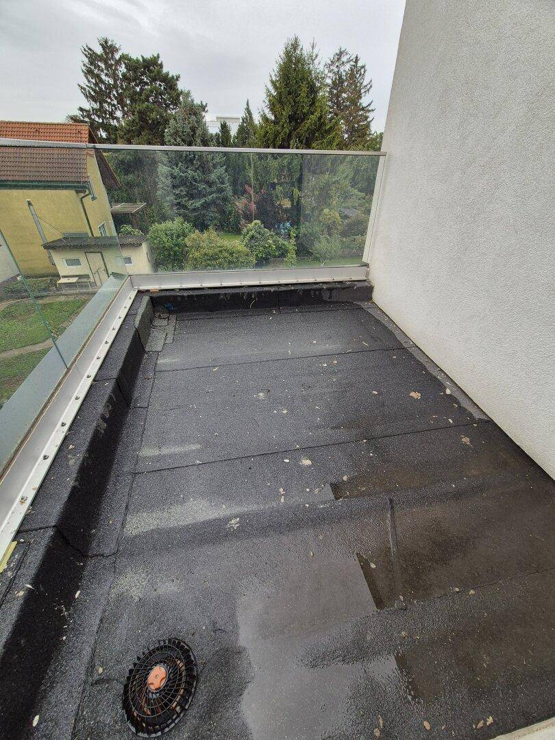 Unfertiger Balkon mit Glasgeländer und Bitumenabdichtung, bietet einen Blick ins Grüne.