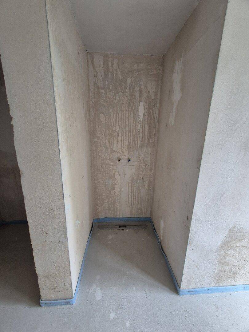 Unfertiger Badezimmerbereich mit vorbereiteten Anschlüssen für Dusche oder Toilette im Rohbauzustand.