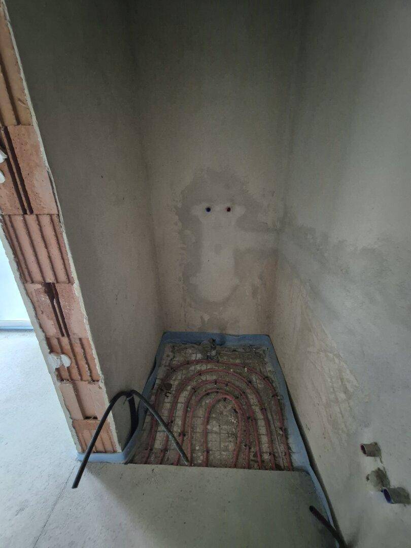 Kleiner Badezimmerbereich im Rohbau mit sichtbarer Fußbodenheizung und Wandvorbereitung für Fliesen.