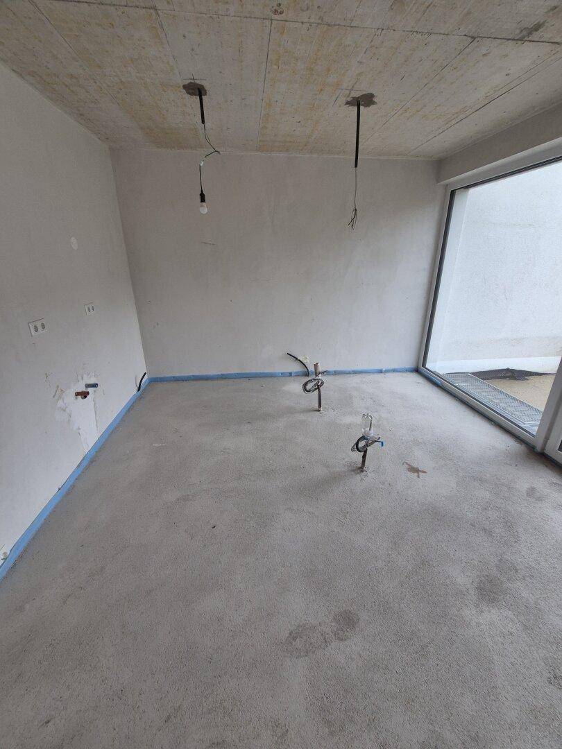 Unfertige Küche mit Anschlüssen für Spüle und Geschirrspüler, hell durch großes Fenster.