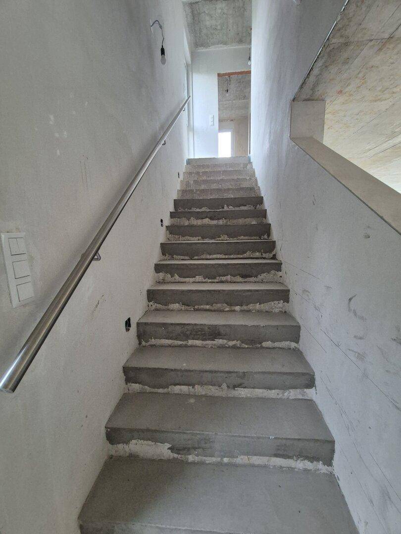 Treppenhaus im Rohbau mit Betonstufen und einfachem Handlauf, führt in obere Etagen des Neubaus.