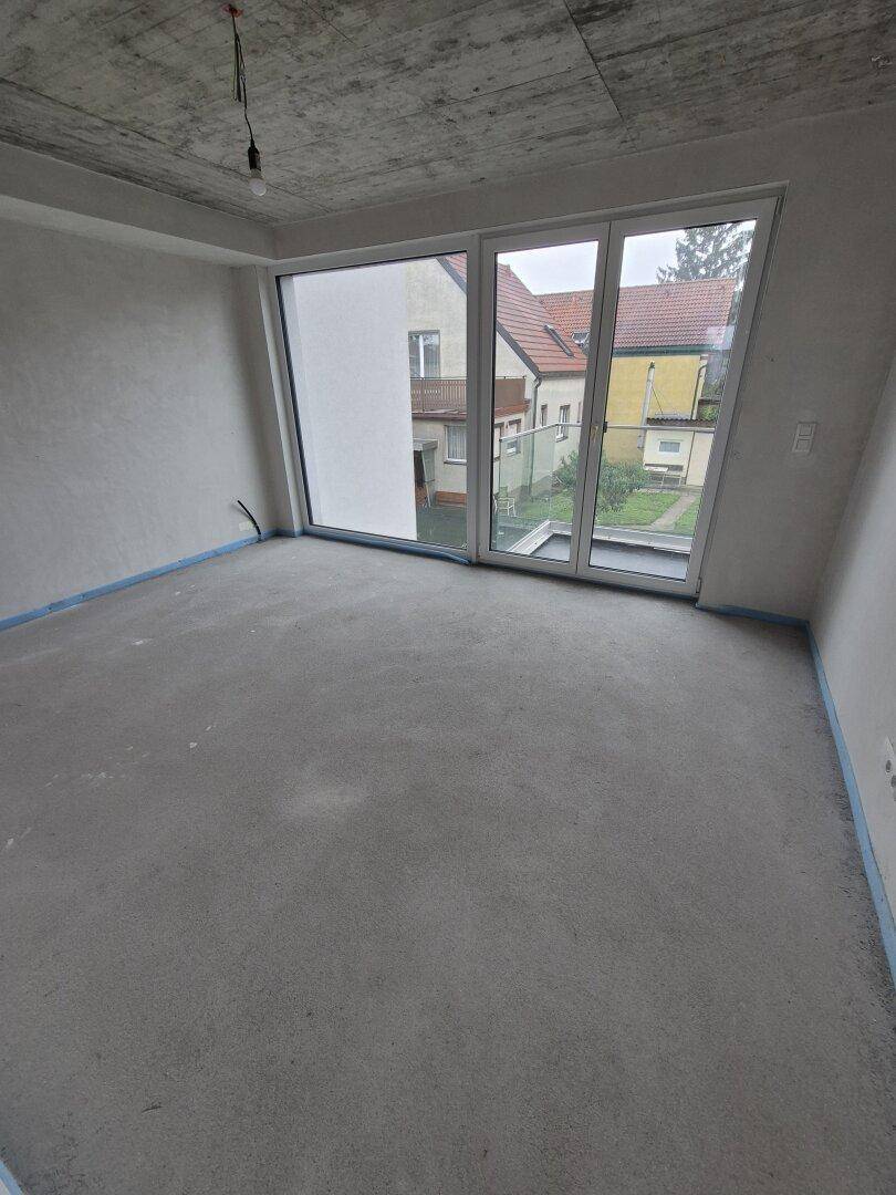 Schlafzimmer im Rohbau mit großen Fenstern und Zugang zu einem möglichen Balkon, viel Licht.