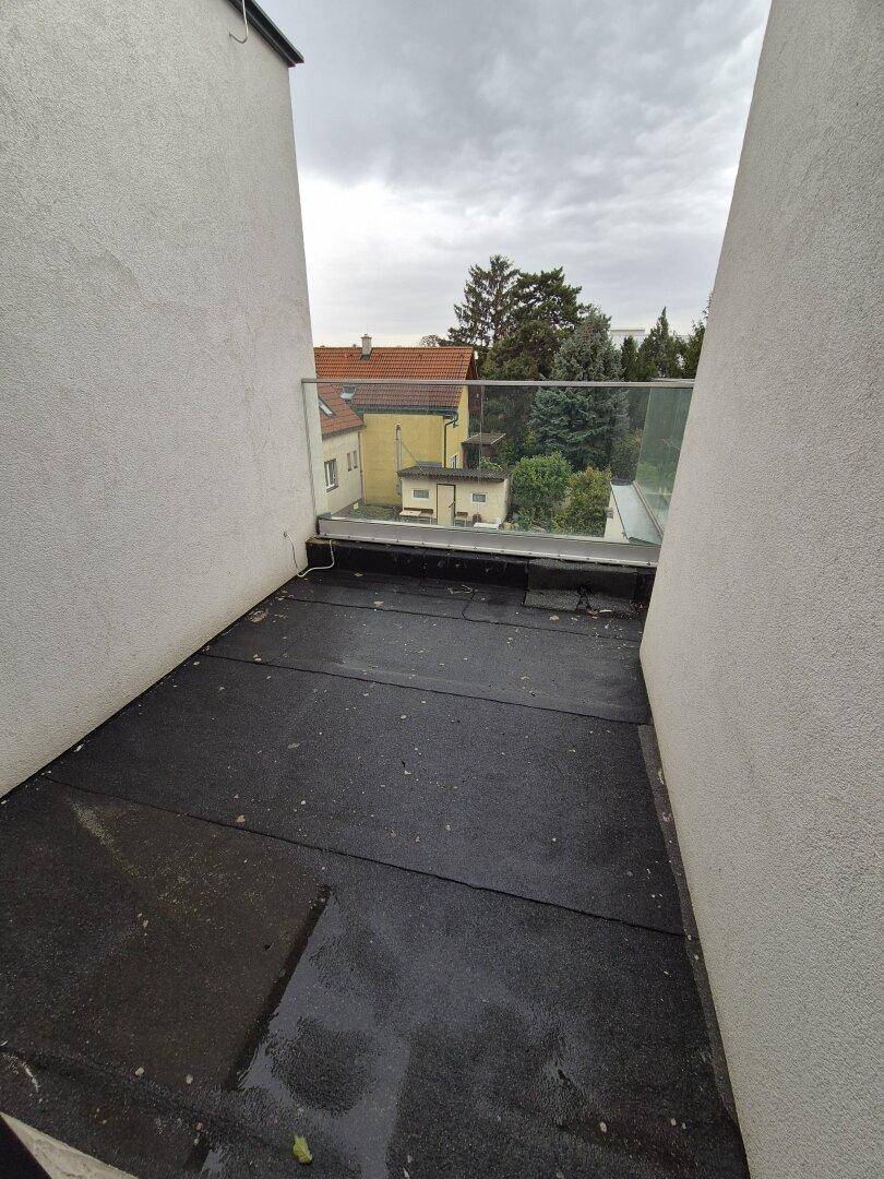 Kleiner Balkon im Rohbau mit Glasgeländer und Blick auf die Nachbarschaft, bereit zur Fertigstellung.