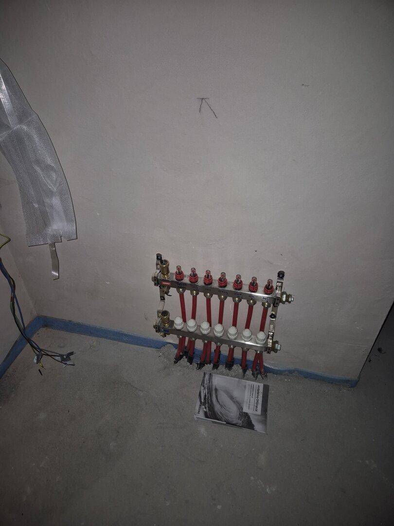 Verteiler für die Fußbodenheizung in einem unfertigen Raum, bereit zur Abdeckung und Fertigstellung.