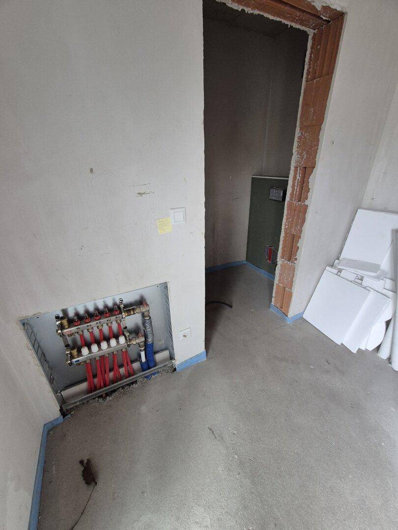 Unfertiger Raum mit Fußbodenheizungsverteiler und offenem Türrahmen, bereit für den Innenausbau.