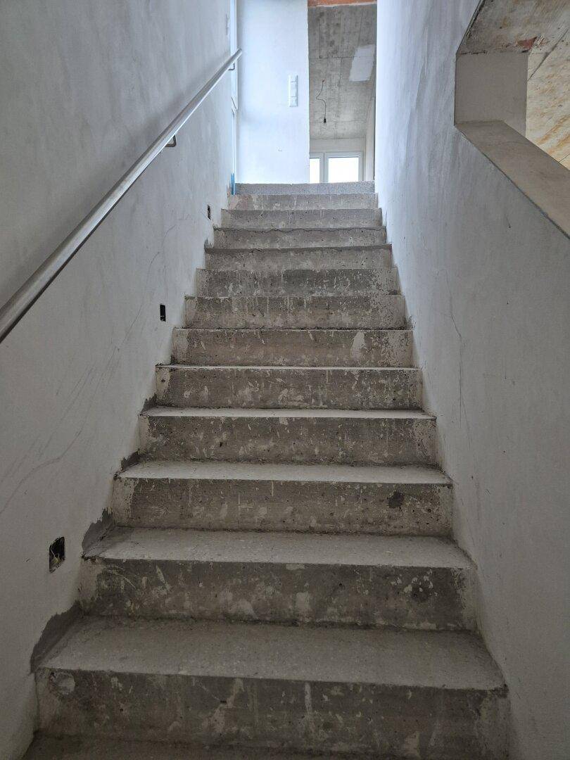 Treppenhaus im Rohbau mit Betonstufen und einfachem Handlauf, führt in obere Etagen des Neubaus.