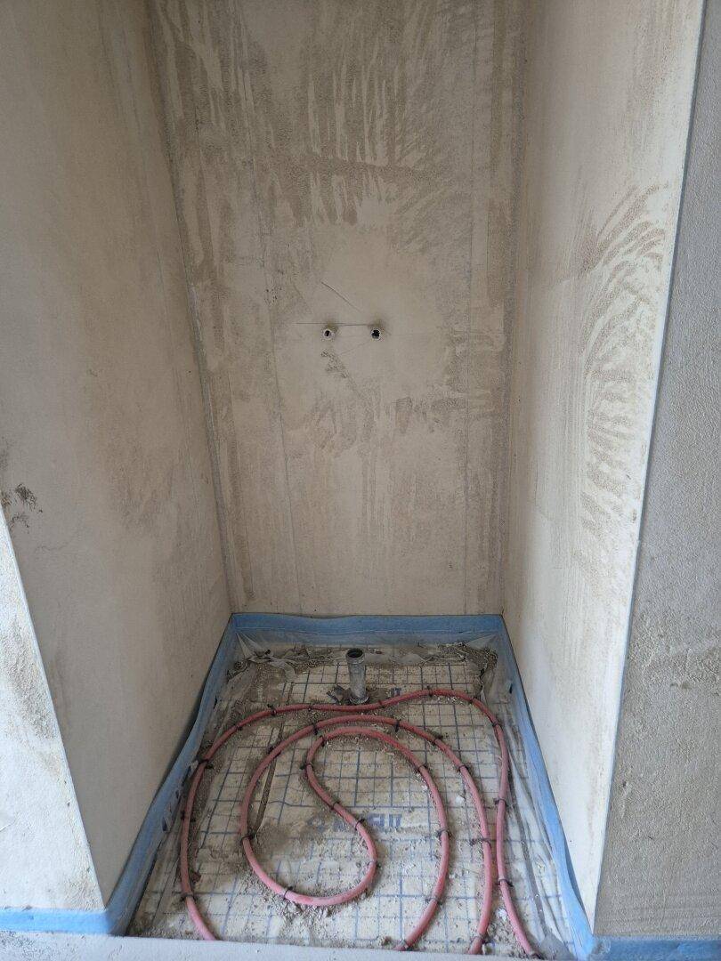 Kleiner Badezimmerbereich im Rohbau mit sichtbarer Fußbodenheizung und Wandvorbereitung für Fliesen.