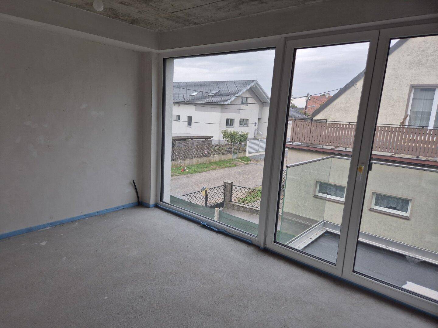 Schlafzimmer im Rohbau mit großen Fenstern und Blick auf die umliegende Nachbarschaft, viel Licht.