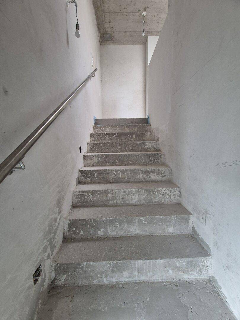 Unfertiges Treppenhaus mit Betonstufen und einem schlichten Metallgeländer.