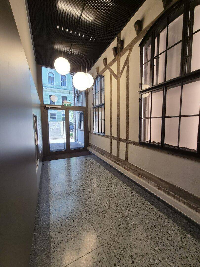 Heller Eingangsbereich mit Terrazzoboden, großen Fenstern und modernen Pendelleuchten an der hohen Decke.