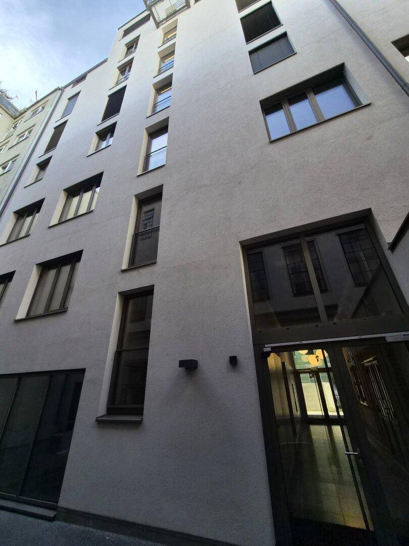Hohe Gebäudefassade mit vielen Fenstern, einigen Rollläden und einer modernen Architektur.