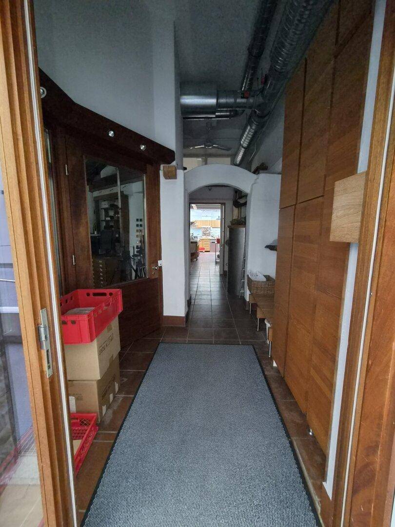 Langer Flur mit Terrakotta-Fliesenboden, Holzverkleidungen und sichtbaren Lüftungsrohren an der Decke.