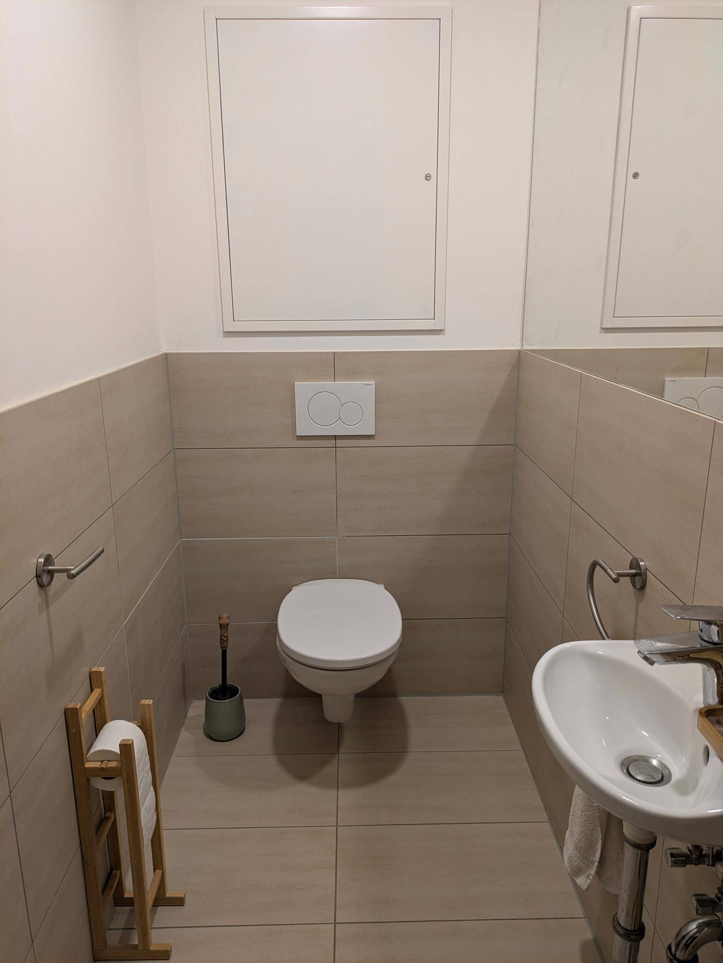 Separates Gäste-WC mit Wand-WC, kleinem Waschbecken und beigefarbenen Fliesen.