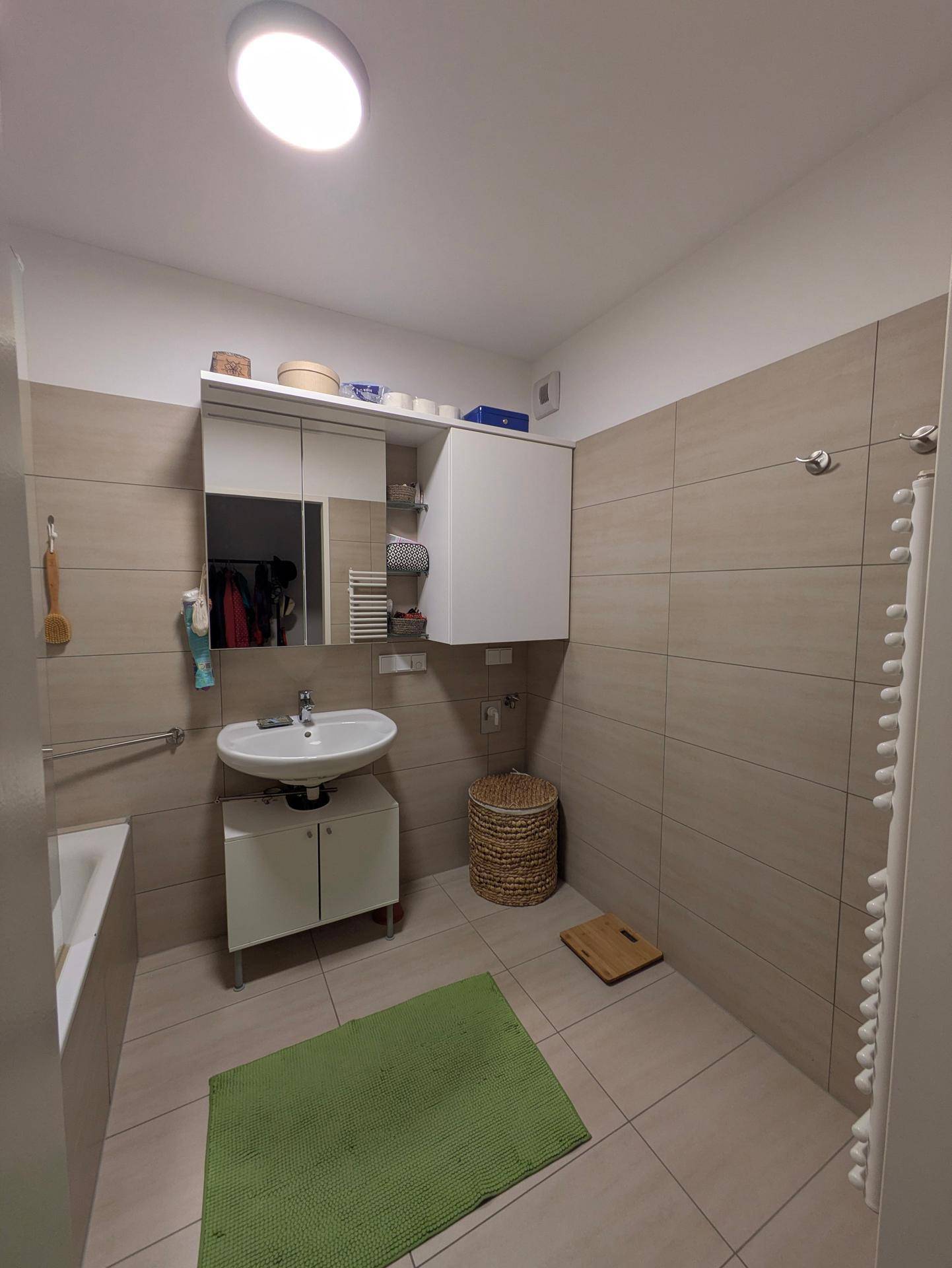 Modern gefliestes Badezimmer mit Waschbecken, Spiegelschrank und Badewanne.