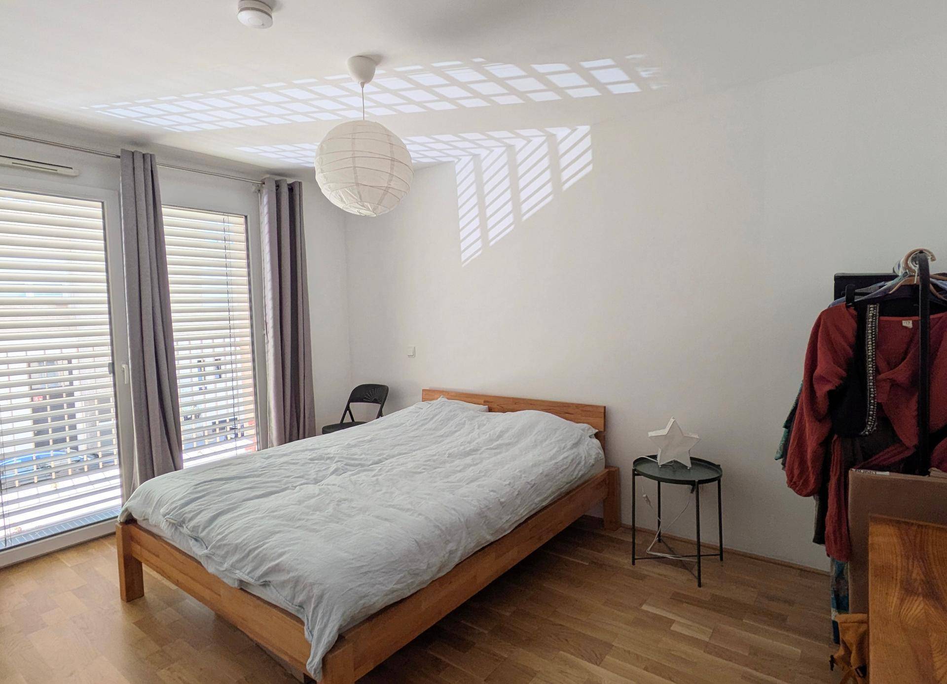 Helles Schlafzimmer mit Holzbett, Parkettboden und Zugang zu einem Balkon oder einer Loggia.
