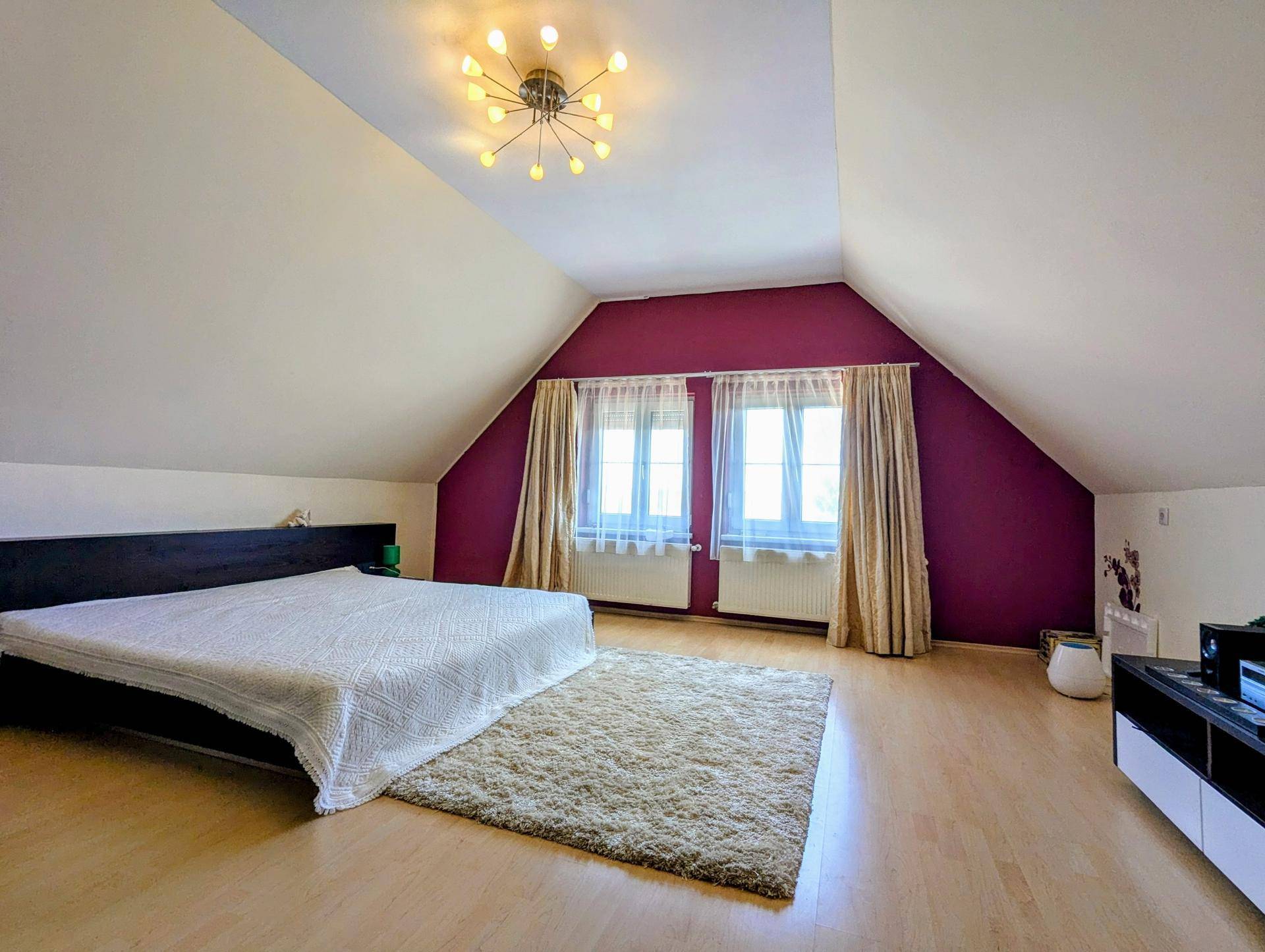 Helles Dachgeschoss-Schlafzimmer mit schrägen Decken, großem Bett und zwei Fenstern.