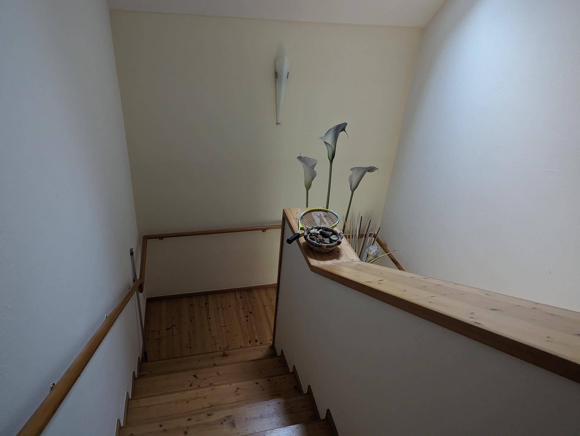 Holztreppe mit schlichtem Geländer und dekorativen Elementen, die die Etagen verbindet.