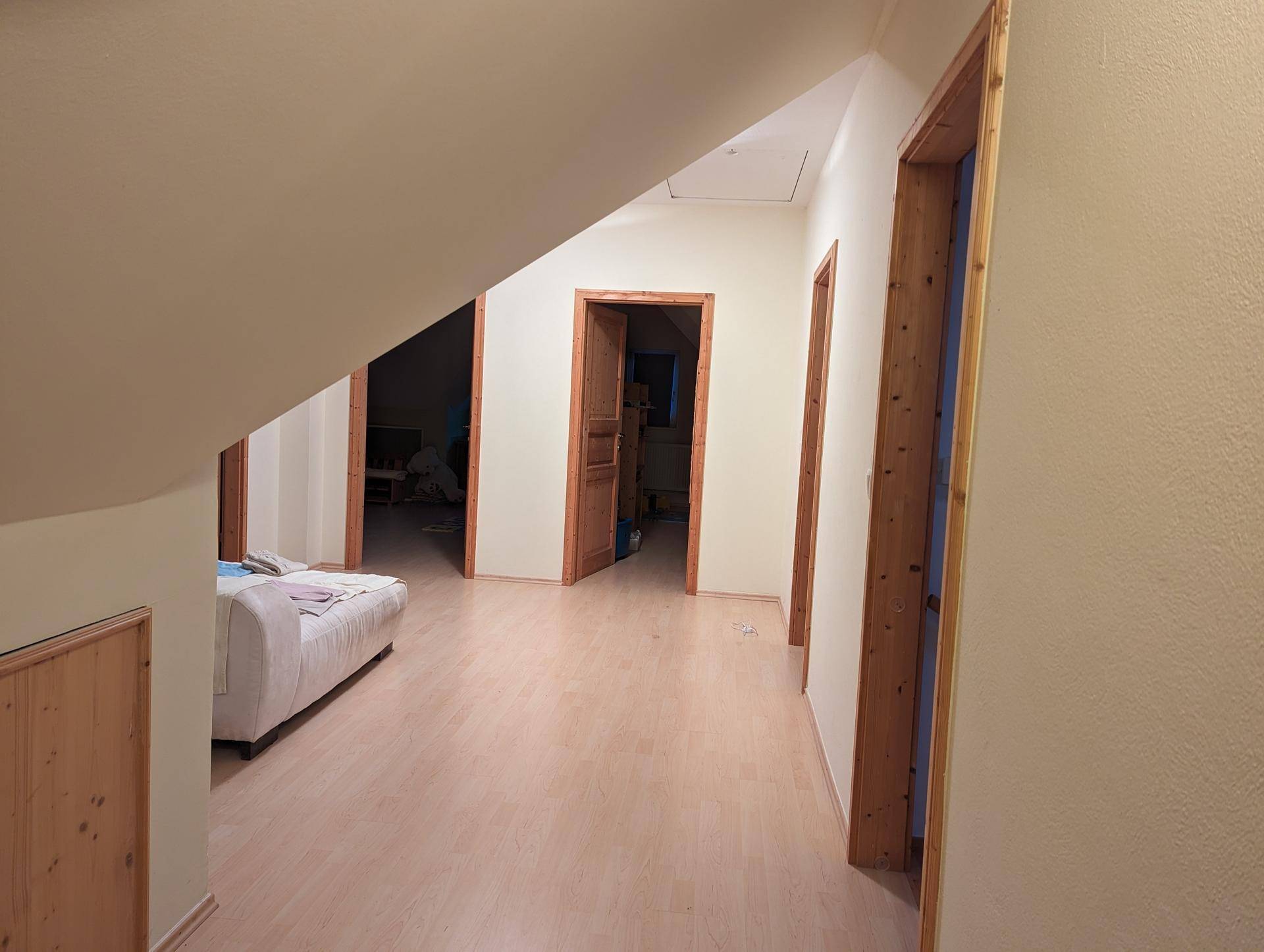 Dachgeschoss-Flur mit Holztüren und hellem Laminatboden, der zu weiteren Räumen führt.