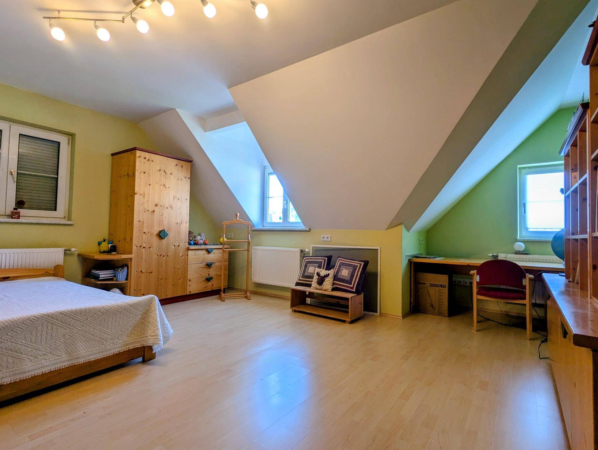Dachgeschoss-Schlafzimmer mit grünen Wänden, schrägen Decken und Holzmöbeln.
