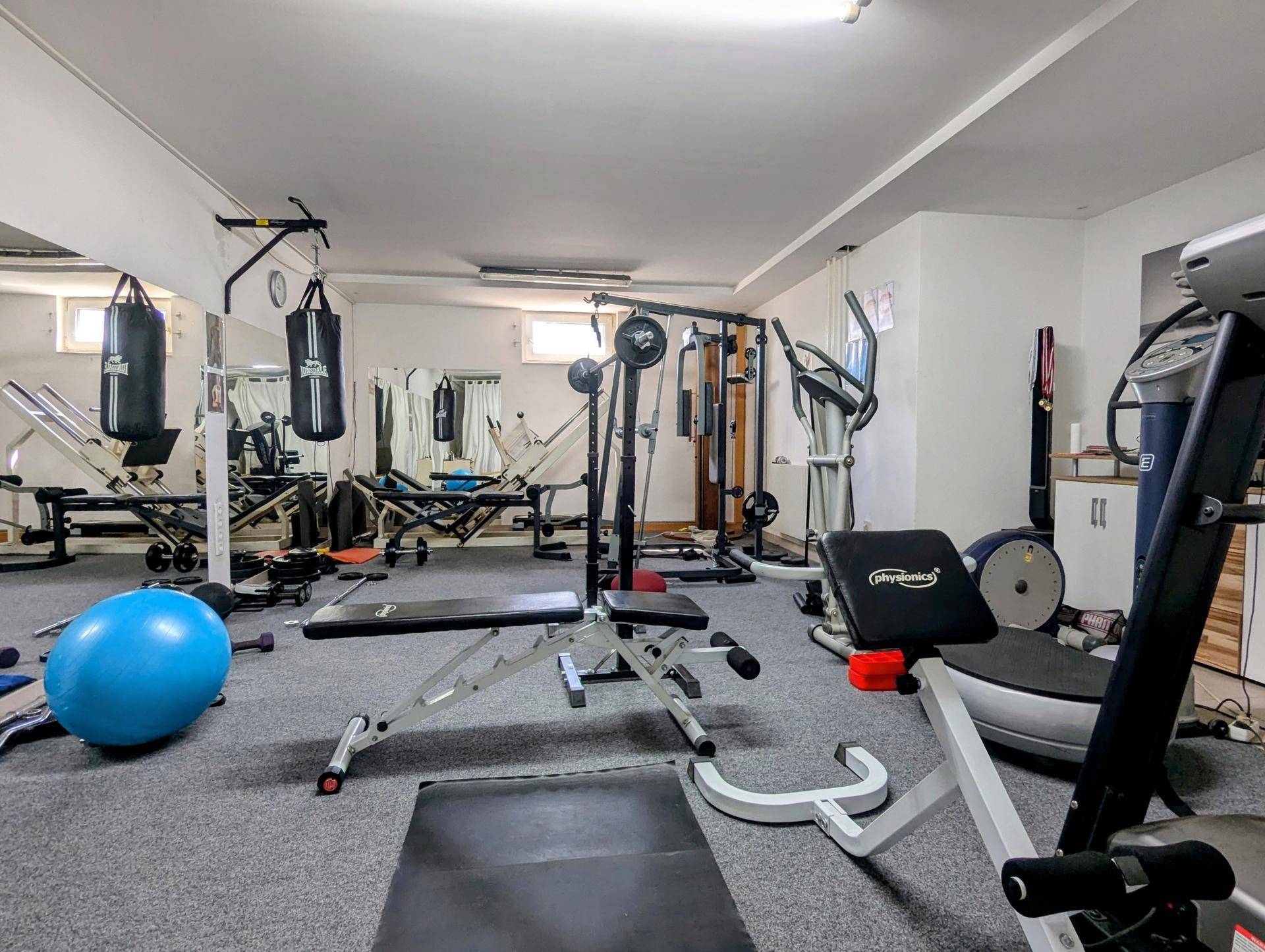 Gut ausgestatteter Fitnessraum im Keller mit Boxsäcken und Hantelbänken.