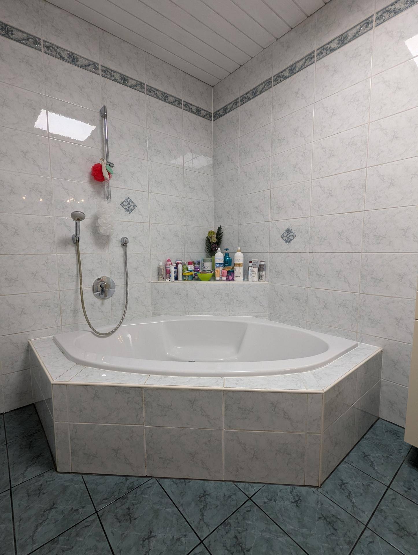 Badezimmer mit Eckbadewanne und hellgrauen Fliesen an Wänden und Boden.