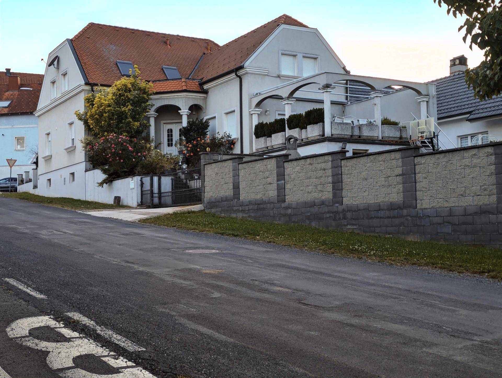 Seitenansicht des Hauses mit Terrassenstruktur und einer Steinmauer entlang der Straße.